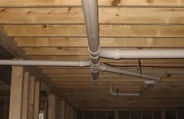 Gray PVC pipes running across a wooden ceiling in a basement.