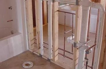 Framing and plumbing for a bathroom remodel; pipes and studs visible.