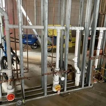 Plumbing pipes and fittings installed within a metal stud wall during construction.