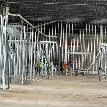 Interior of a building under construction, metal stud framing. Workers visible.