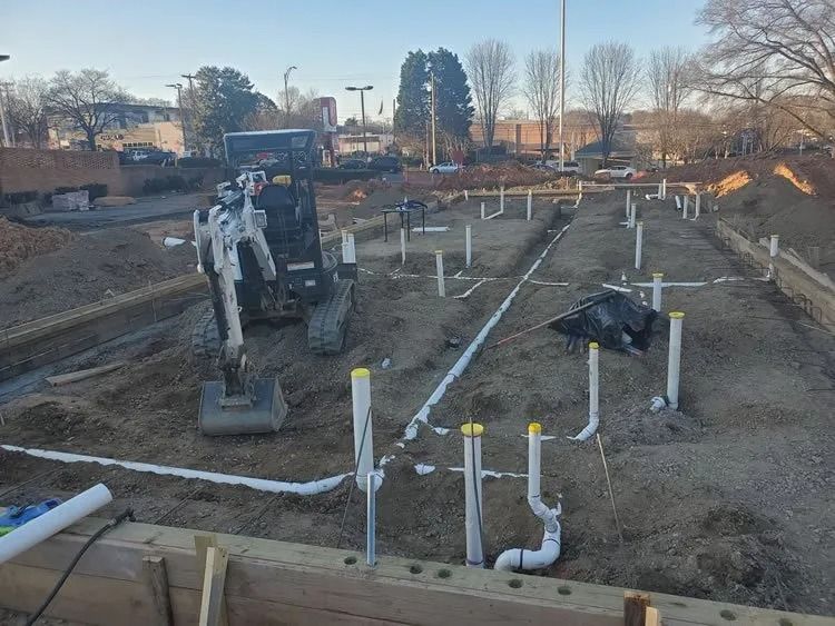 Construction site with a small excavator and white pipes laid in trenches.