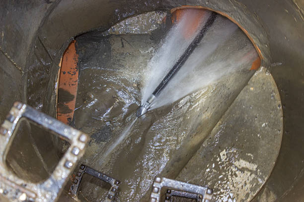 A high-pressure water hose cleaning the interior of a concrete sewer manhole.