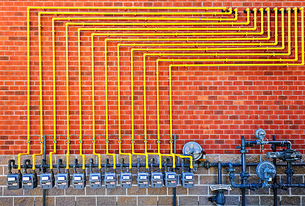 A row of gas meters on a brick wall with yellow pipes branching upward in a structured pattern.