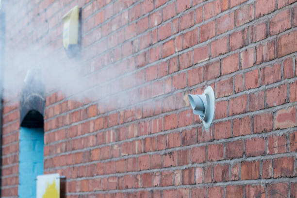 A brick wall showing two vents, with steam venting from the left side.