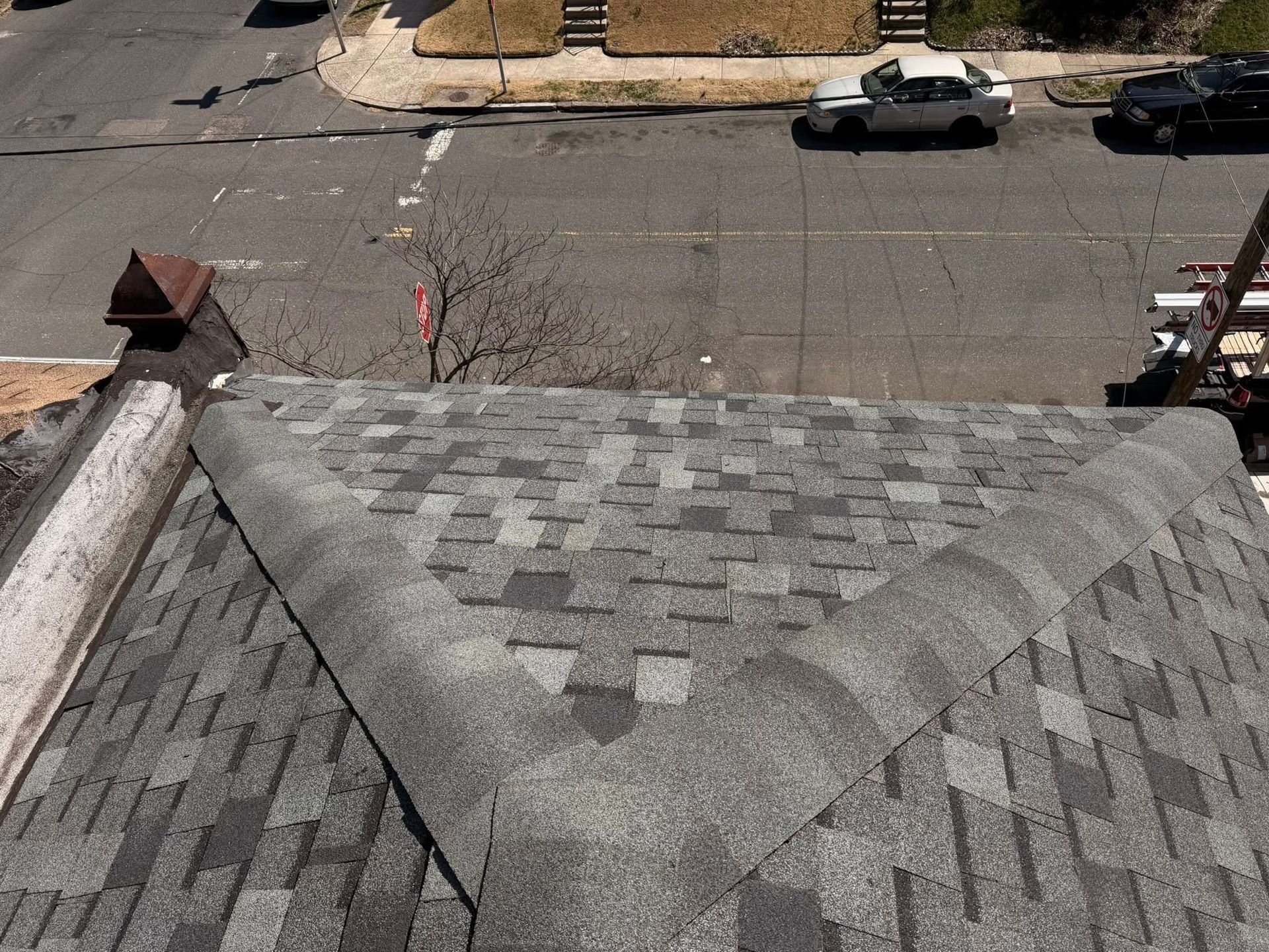 Gray shingled roof with a triangular ridge overlooking a street with parked cars and a sidewalk
