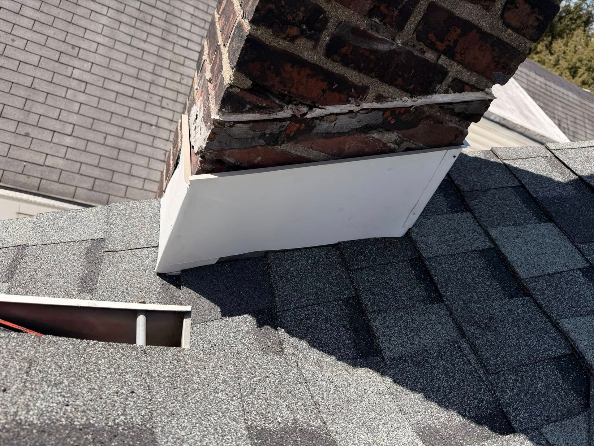 Damaged brick chimney base above a gray shingled roof with exposed interior bricks