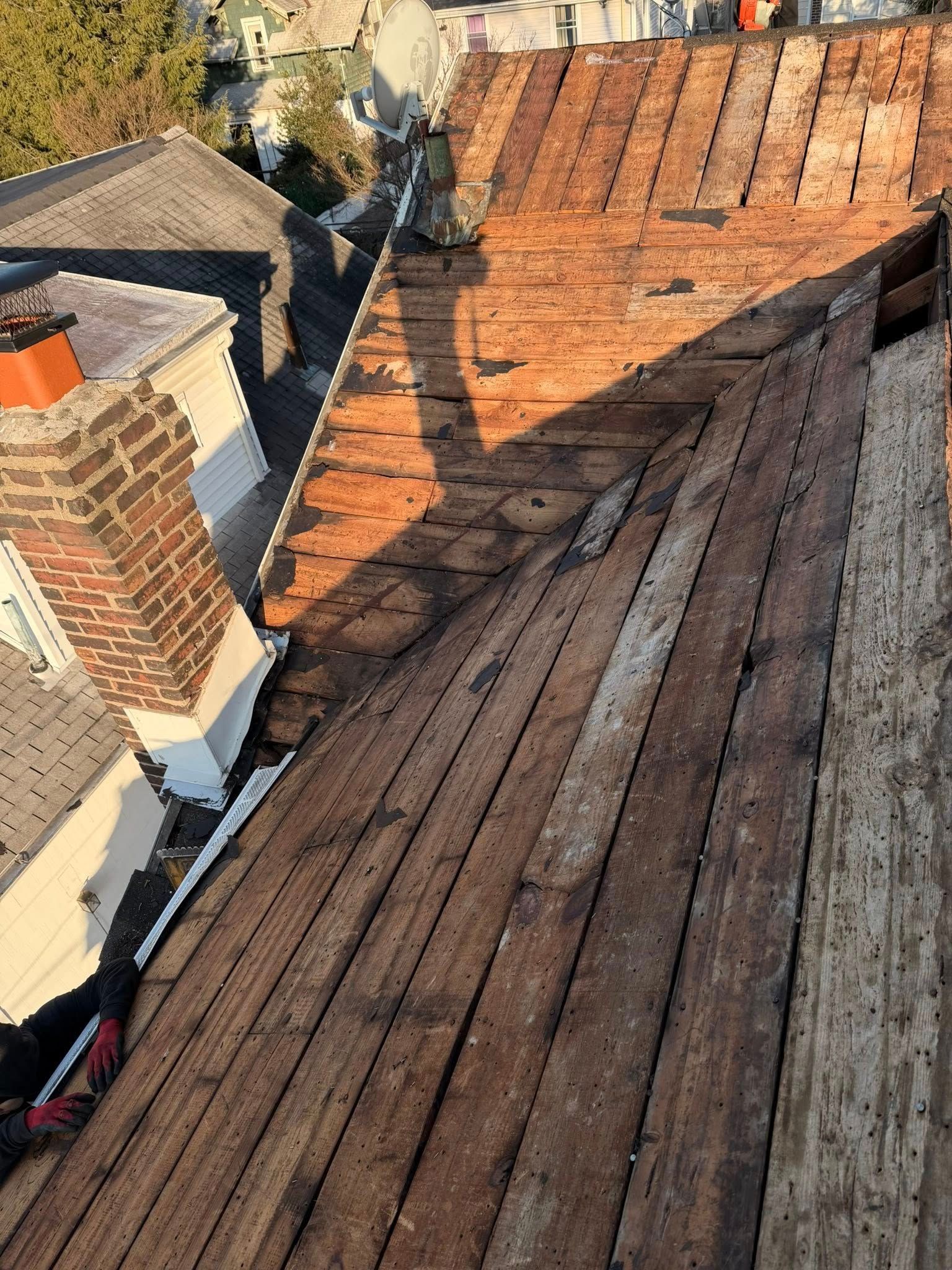 Rooftop view of weathered wooden shingles and orange-red tiles beside brick chimneys in sunlight