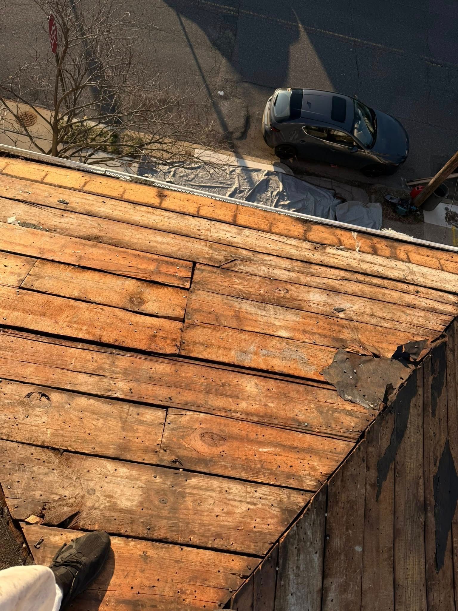 Steep rooftop with weathered orange shingles overlooking a street with parked cars below