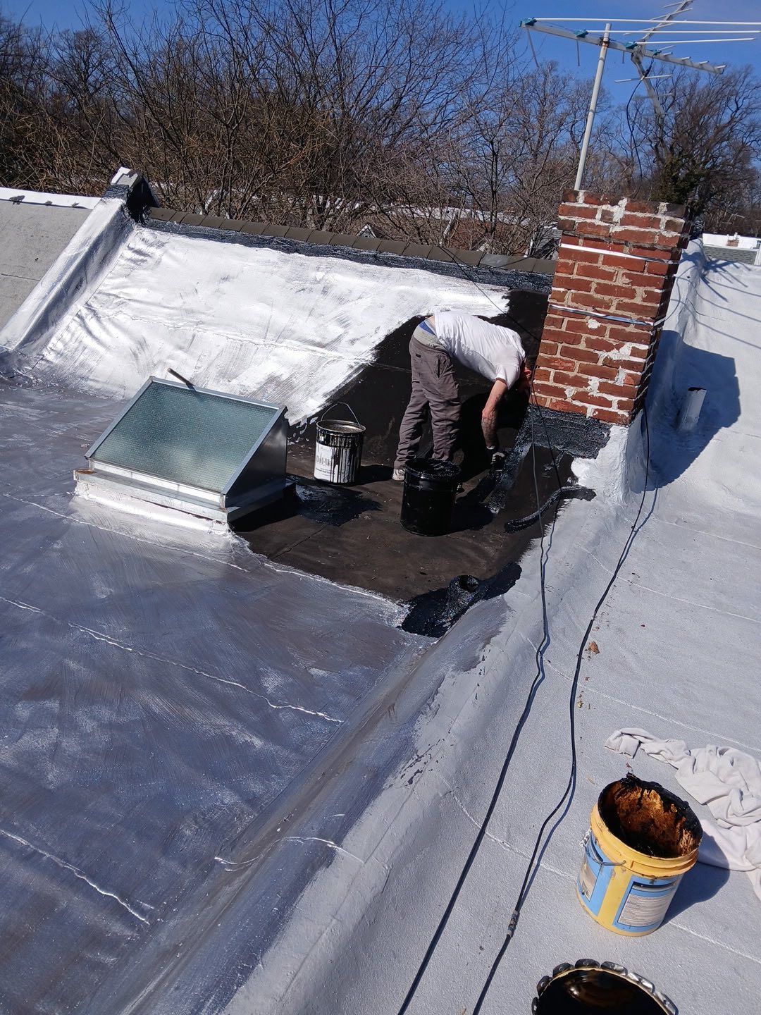 Worker on a metal roof repairing a vent near a brick chimney on a sunny day