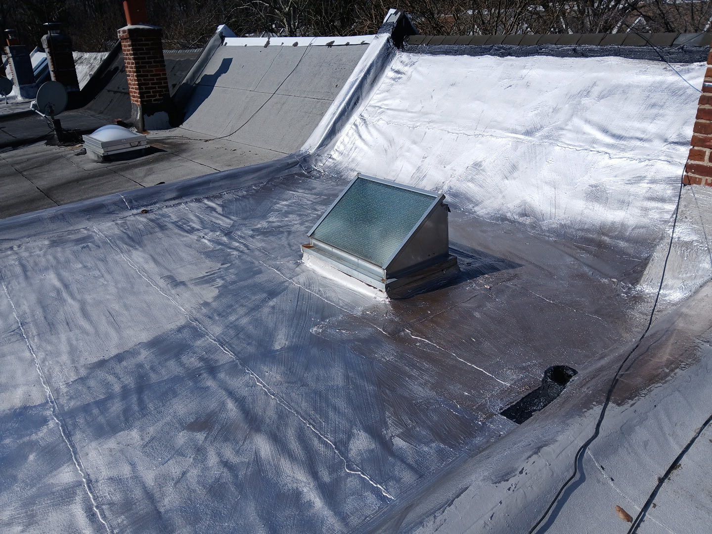 Flat rooftop with a small skylight and patches of snow on a sunny day.