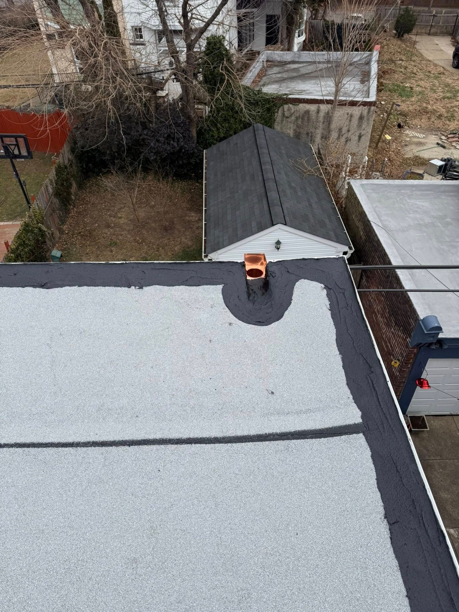 Rooftop with gray membrane roofing, dark ridge, and vent pipe, viewed from above.