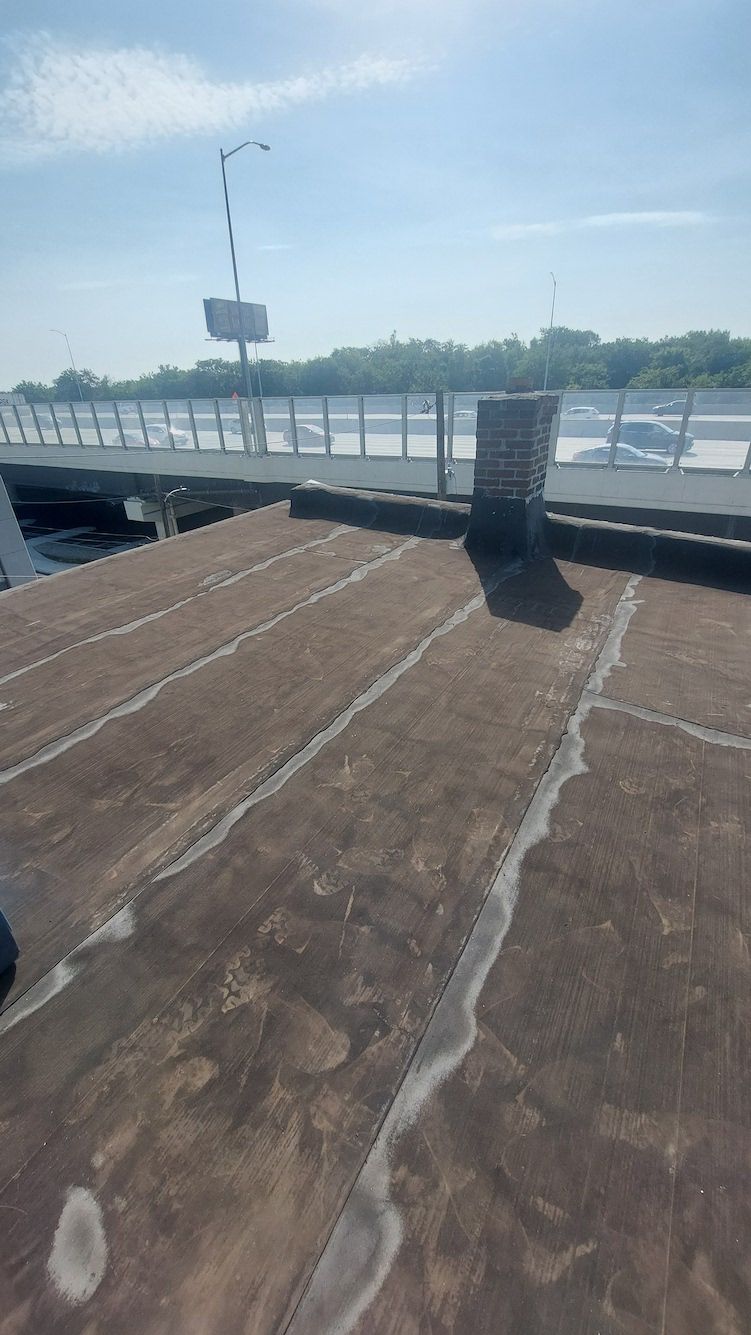 Rooftop with a metal railing, weathered brown surface, and distant water under a clear blue sky