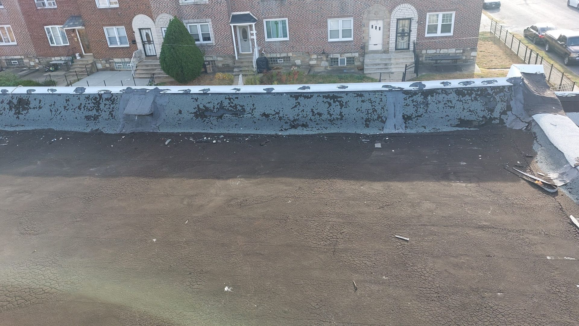 Rooftop with gravel surface and a low stone wall, overlooking brick apartment buildings and trees beyond.