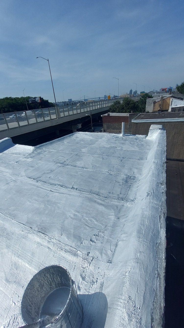 Rooftop with white coating and a small vent, overlooking a road, bridge, and blue sky.