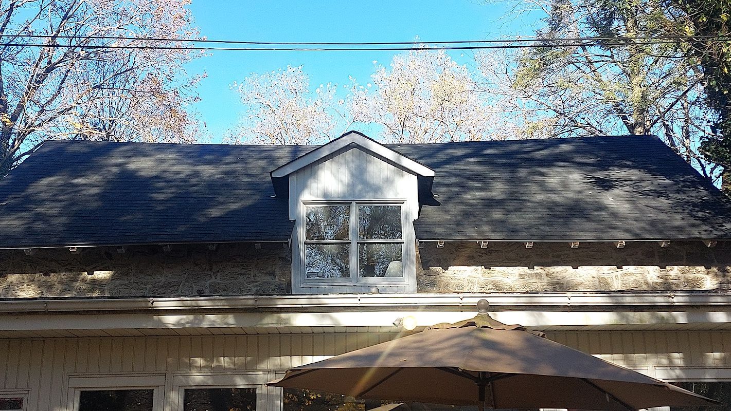 House roof with dormer window under blooming trees and a patio umbrella