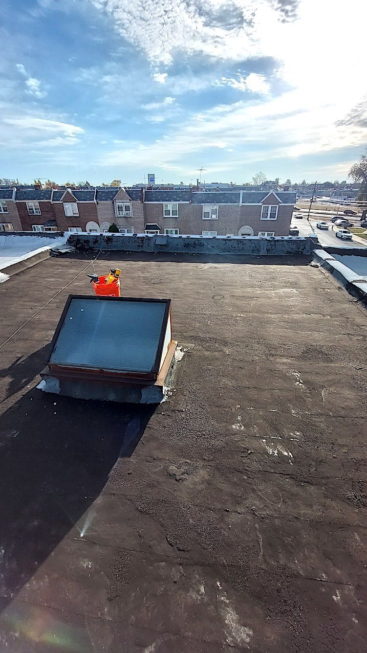Rooftop with flat gravel surface, solar panel, and brick buildings under a bright blue sky.
