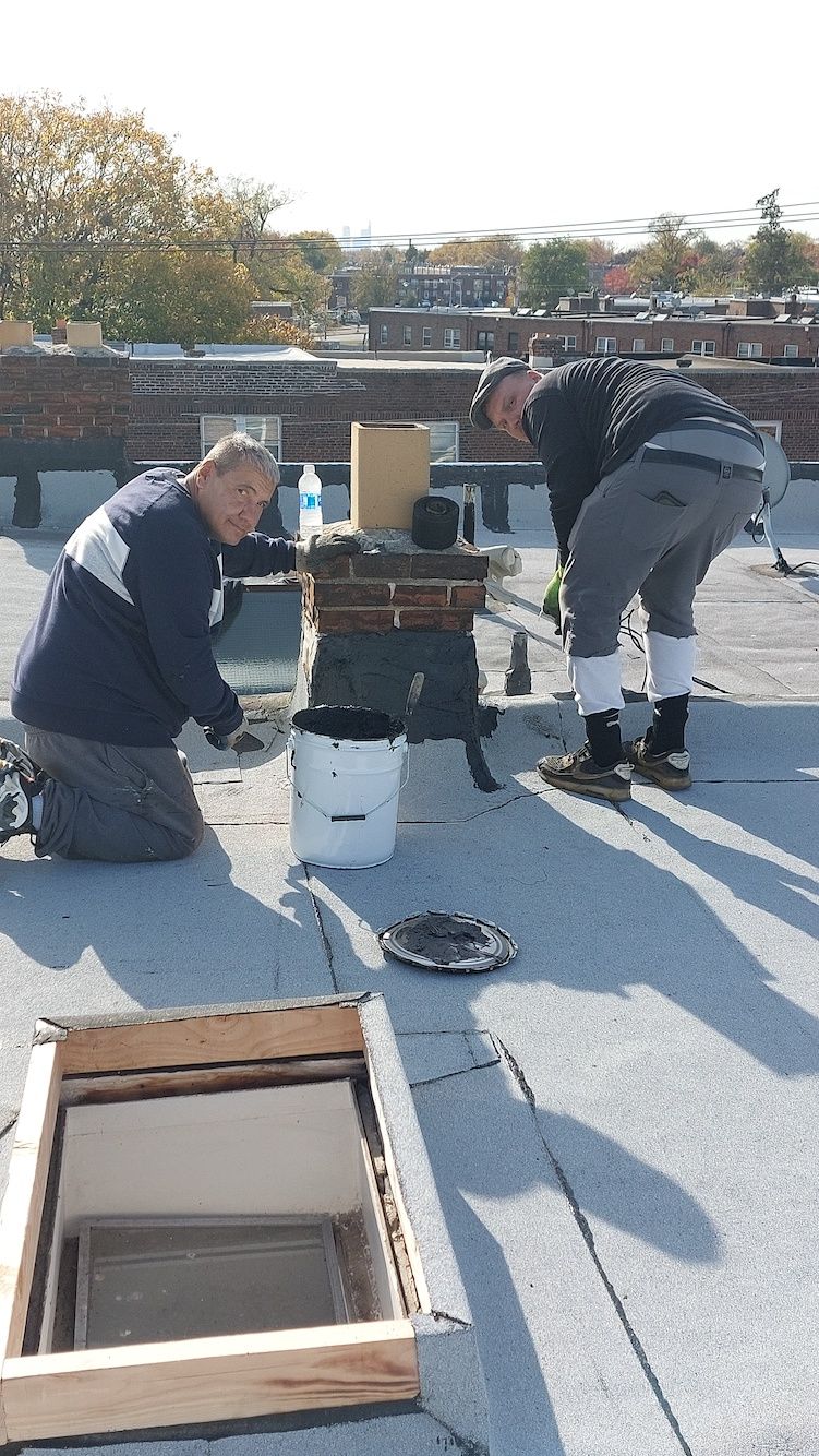 Three people inspect rooftop HVAC units on a flat roof on a clear day.