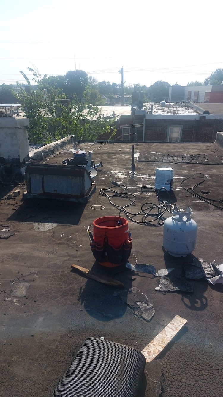 Rooftop with propane tanks, a bucket, a small trailer, and a tire under bright sunlight