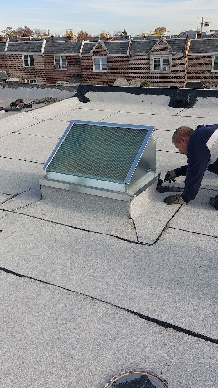 Rooftop skylight with a person crouching beside it on a flat roof.