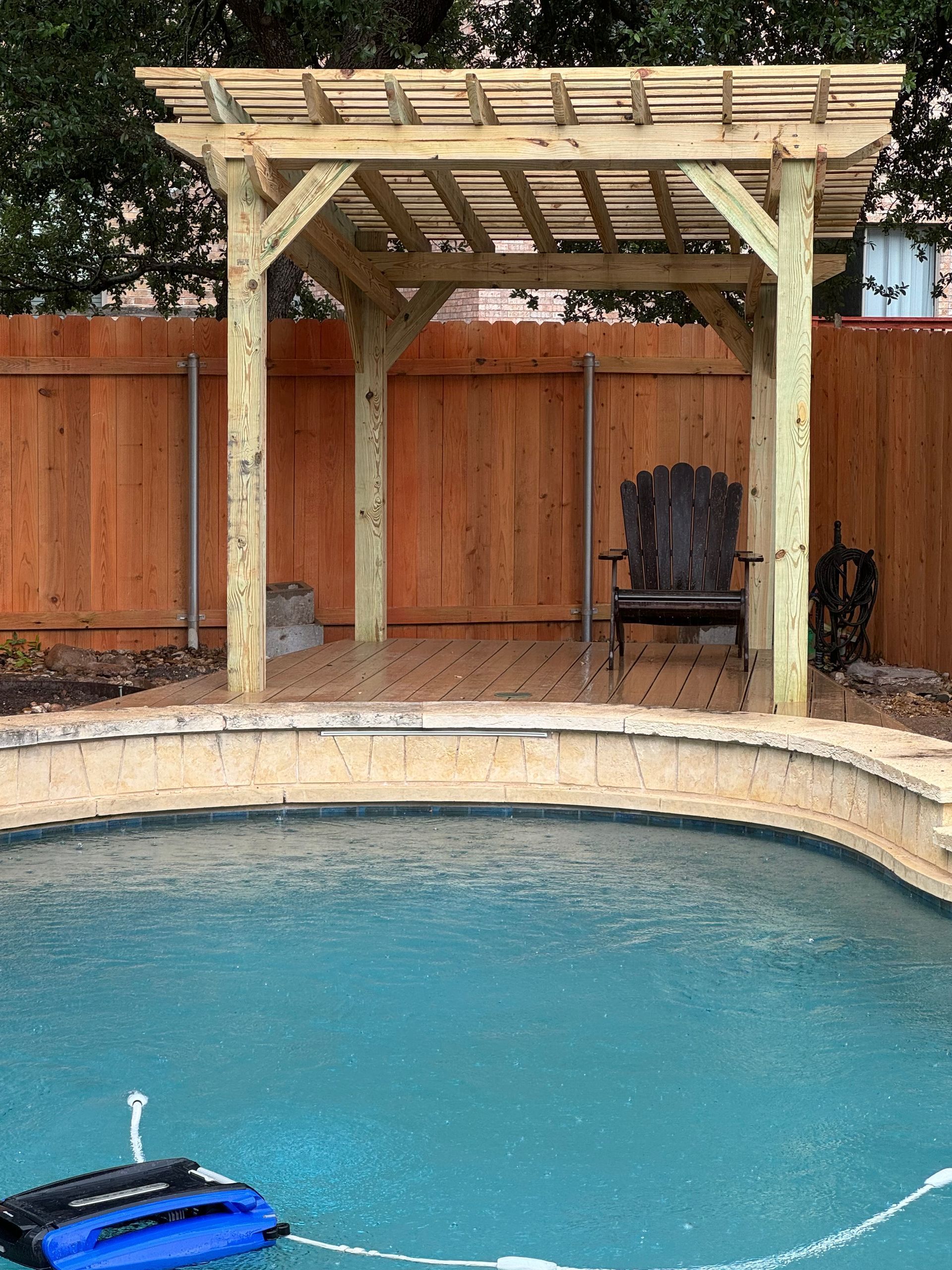 A wooden pergola over a swimming pool with a chair underneath it.