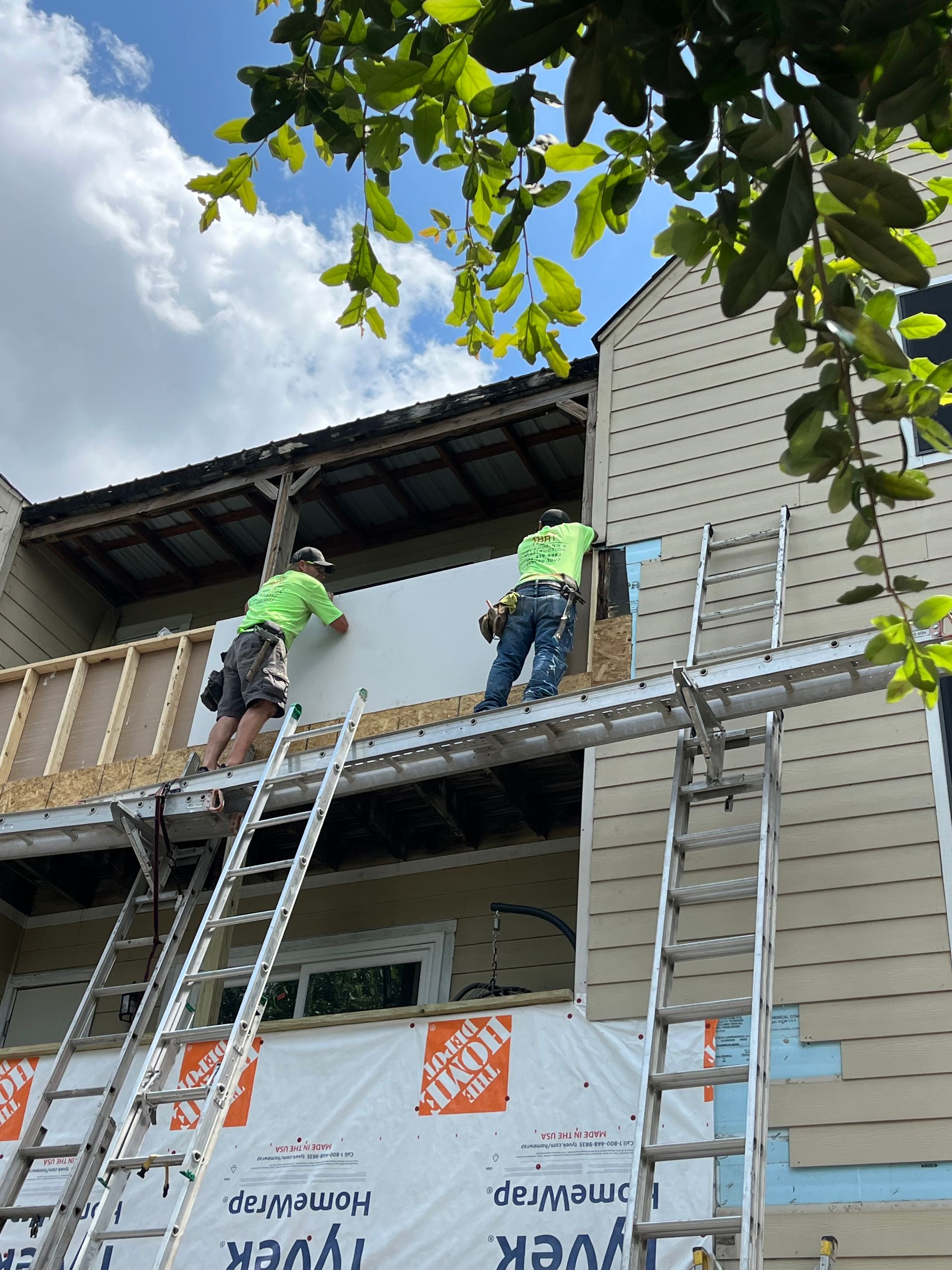 Two men are standing on a scaffolding on the side of a house.