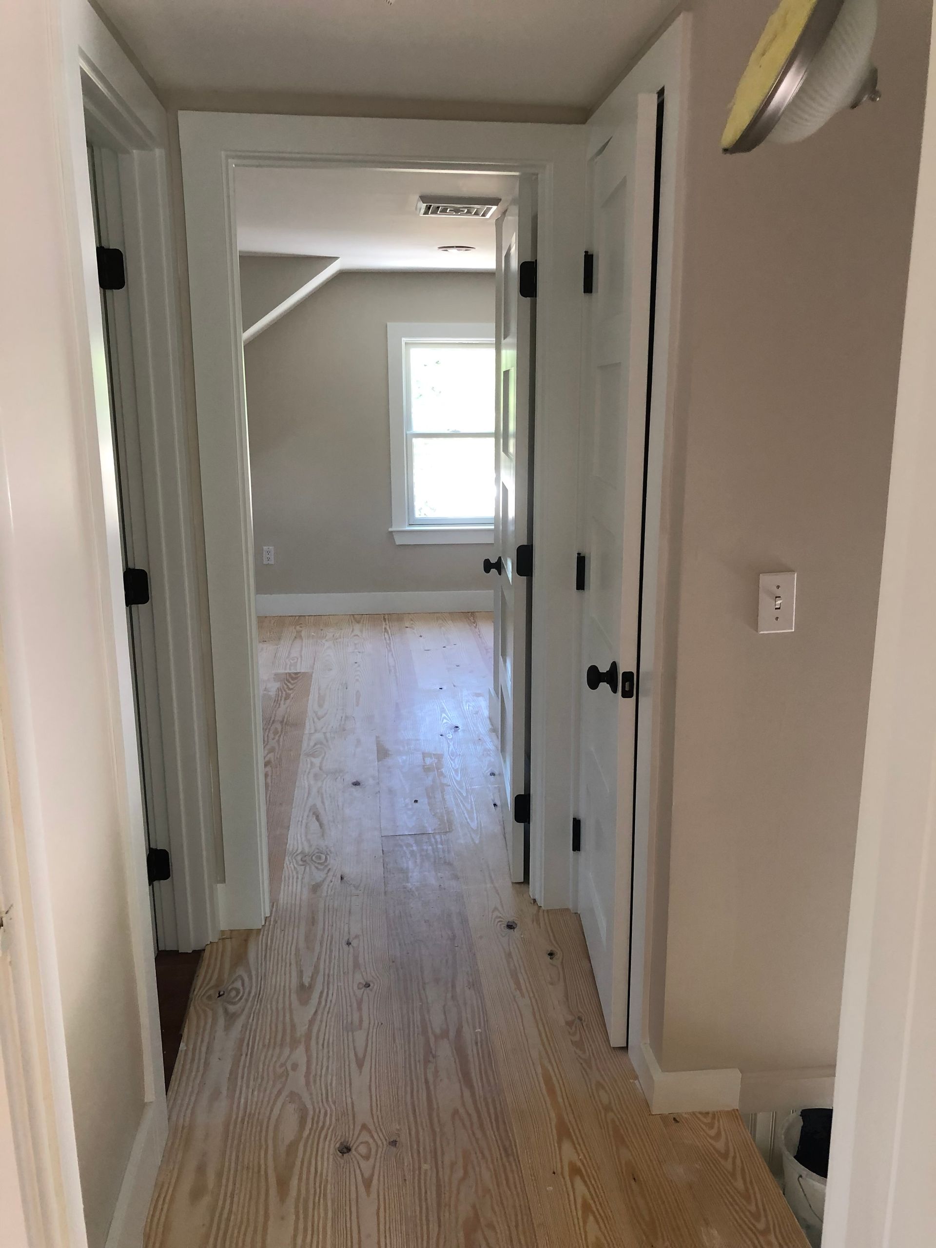 Hallway with light wood floors, white doors, and a bright room at the end.