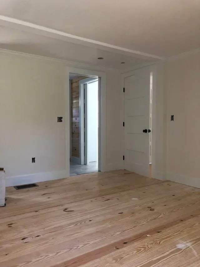 Empty room with light wood floors, white walls, and a doorway leading to another room.