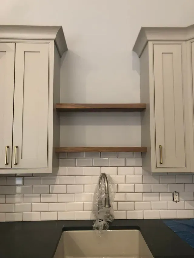 Kitchen with white cabinets, wood shelves, subway tile backsplash, sink, and faucet.