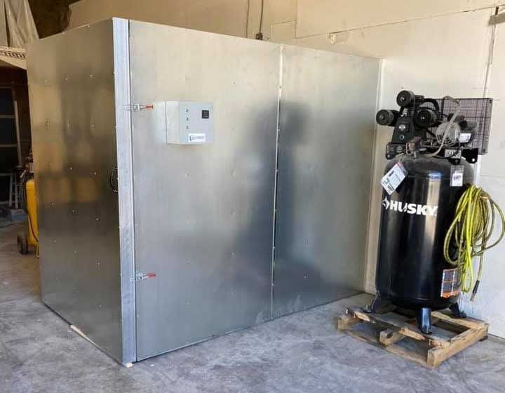A large, metallic-looking storage box with a control panel next to a Husky air compressor in a warehouse setting.