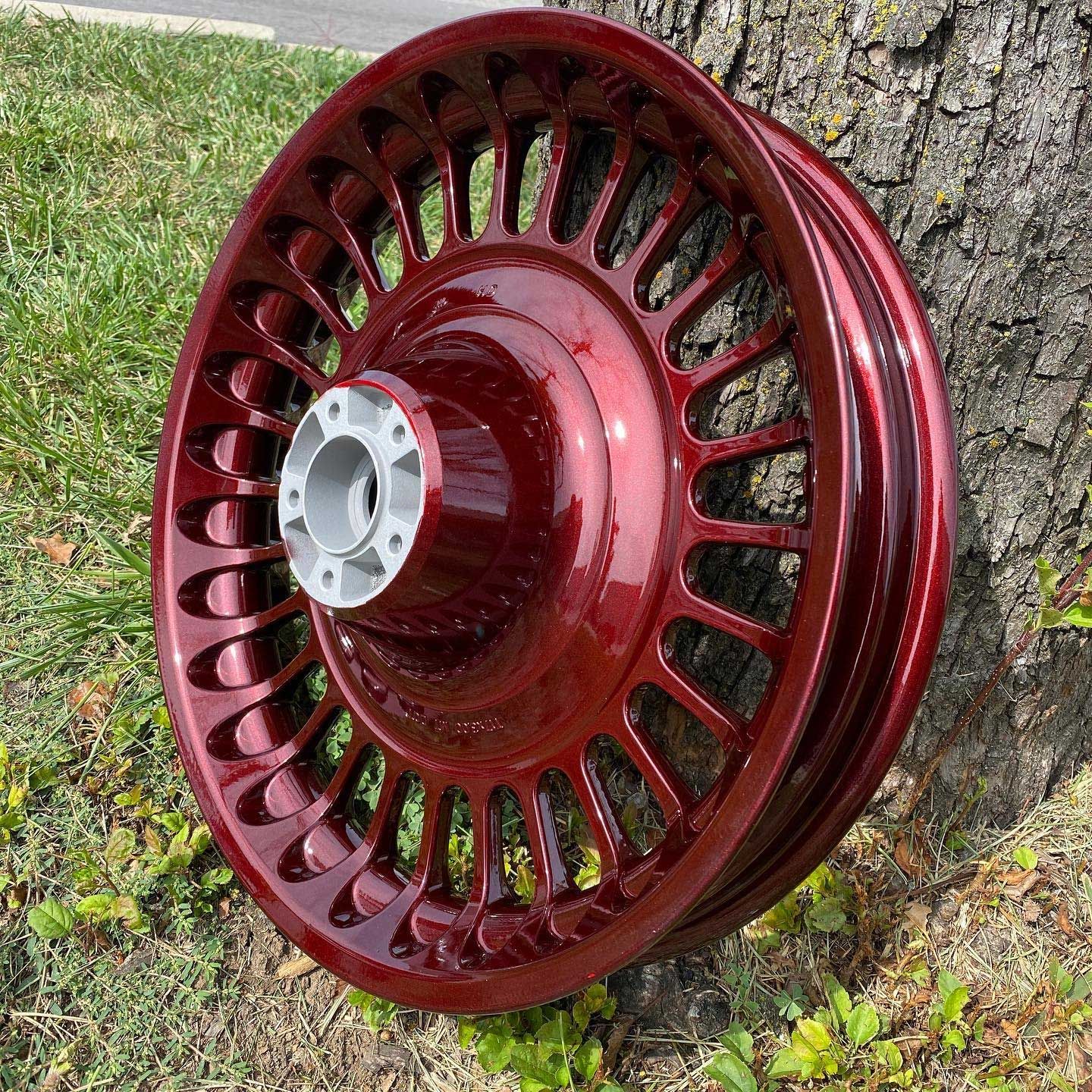 Maroon motorcycle wheel resting on grass next to a tree.