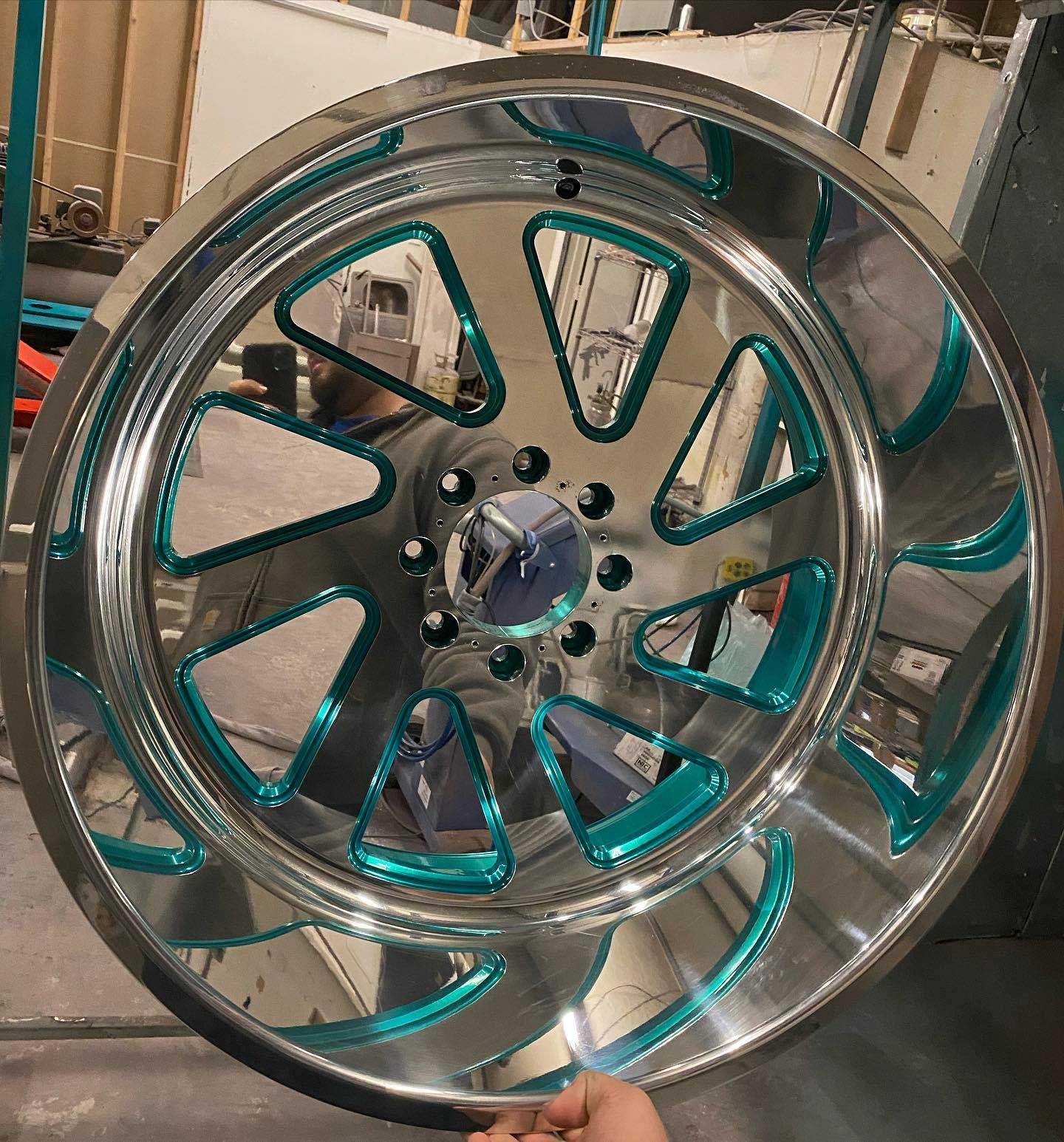 Shiny chrome truck rim with teal accents and a reflective surface.