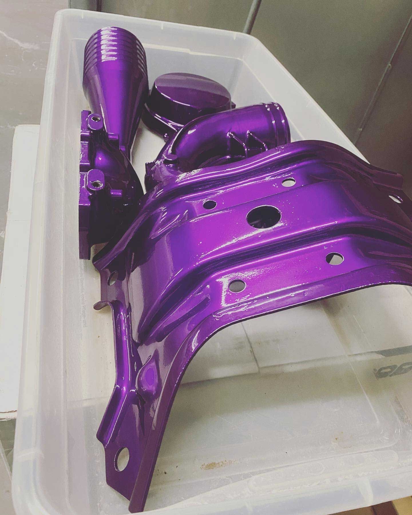 Purple painted car parts in a white container, including brackets and intake components.