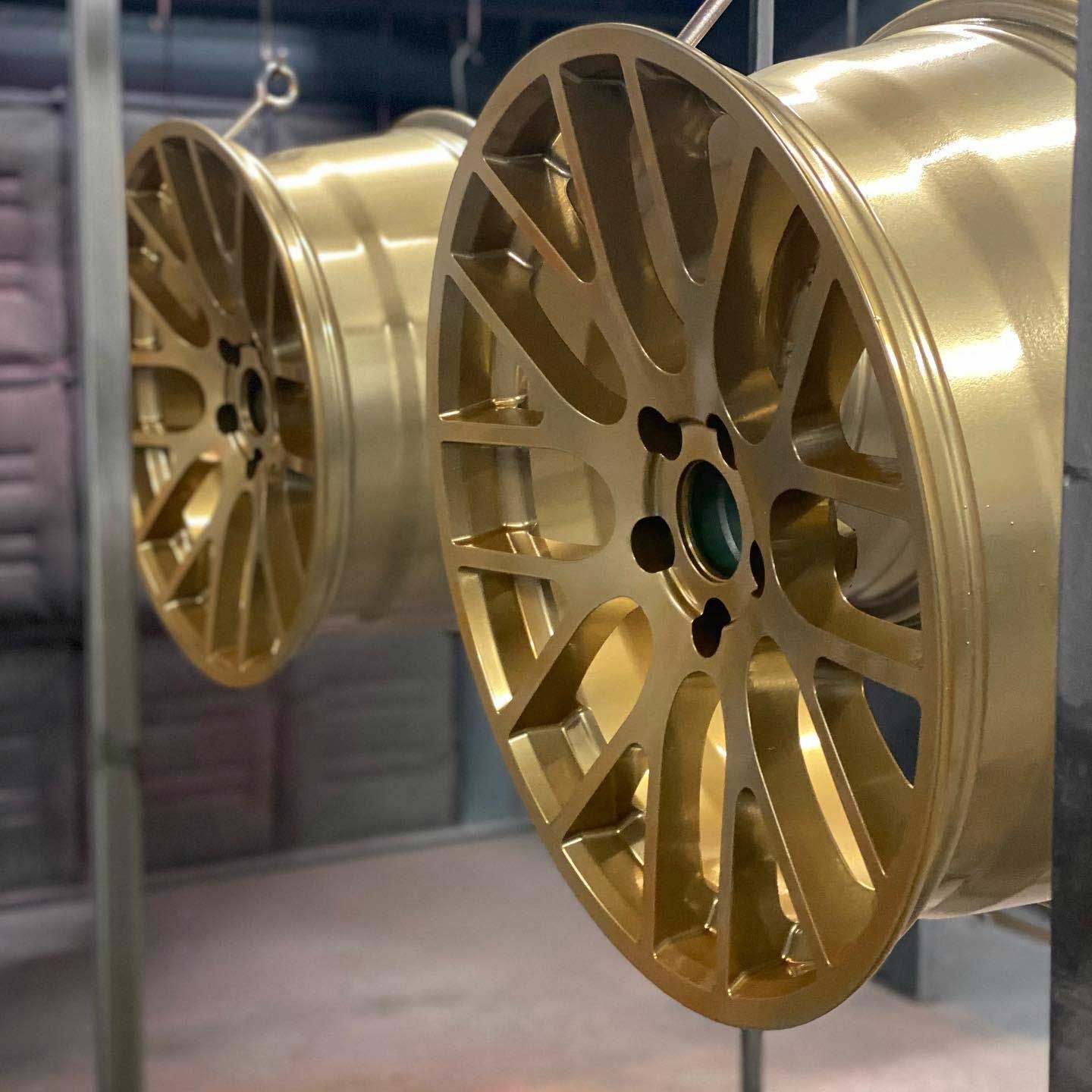 Two gold-painted car wheels hanging from hooks in a workshop.