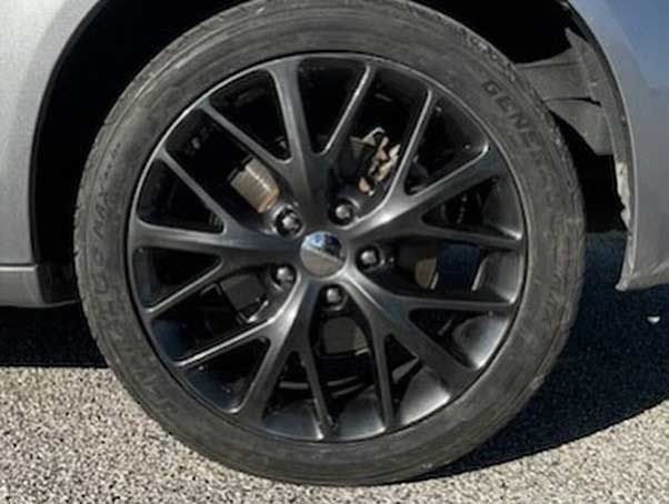 Black car wheel with a black rim and tire on gray pavement.