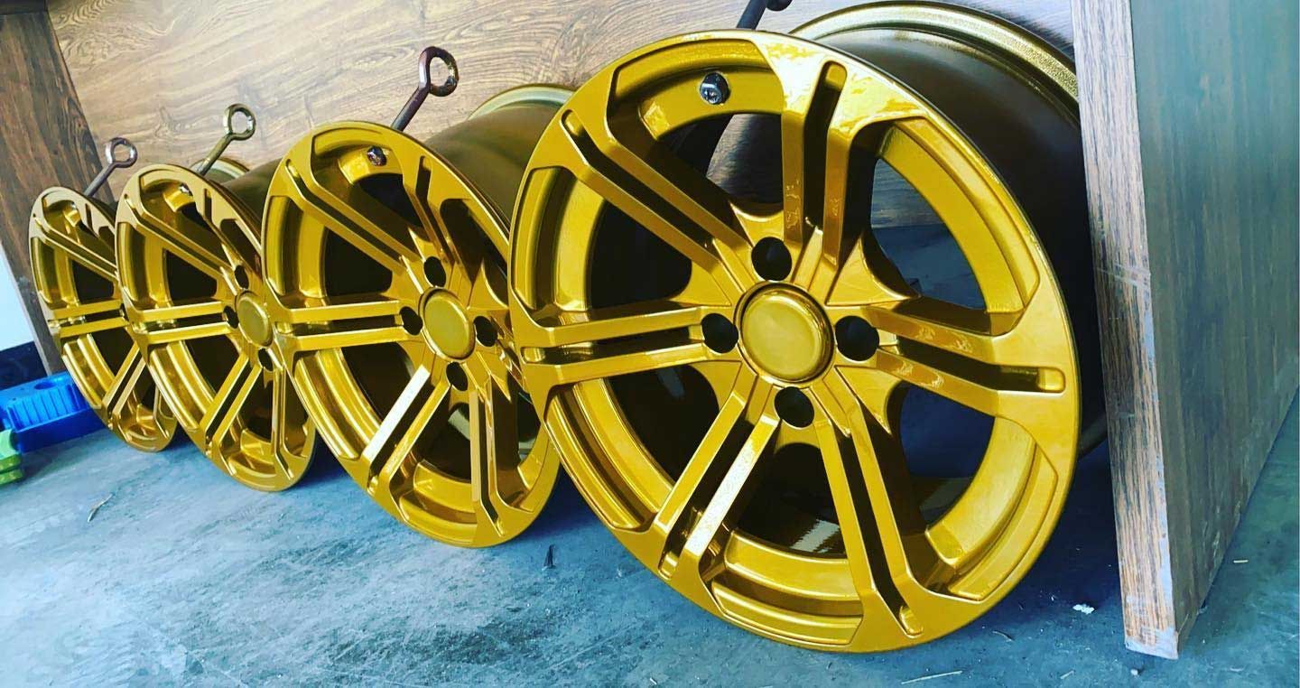 Five gold-colored car wheels lined up on the ground, leaning against a wooden structure.