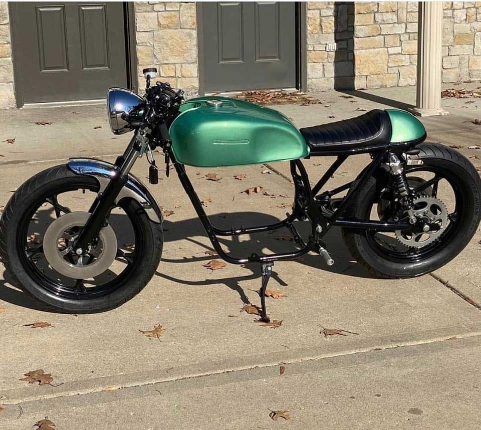 Green cafe racer motorcycle on a concrete surface, black wheels, chrome fenders, and black seat.