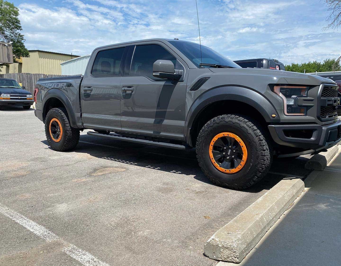 Gray Ford Raptor pickup truck with orange accents parked in a parking lot on a sunny day.