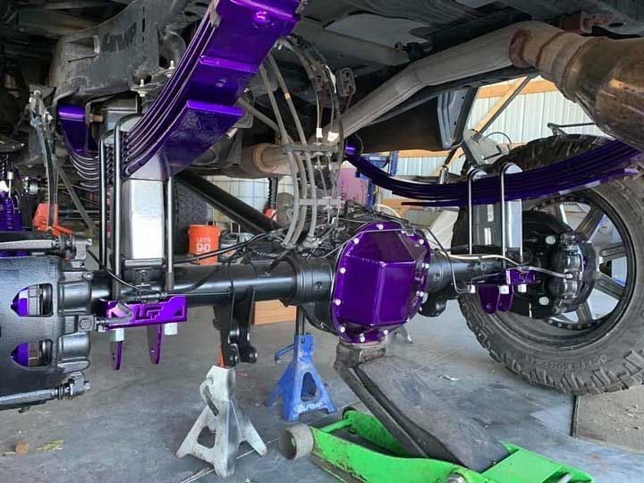 Purple lifted truck suspension with leaf springs and axle, garage setting.