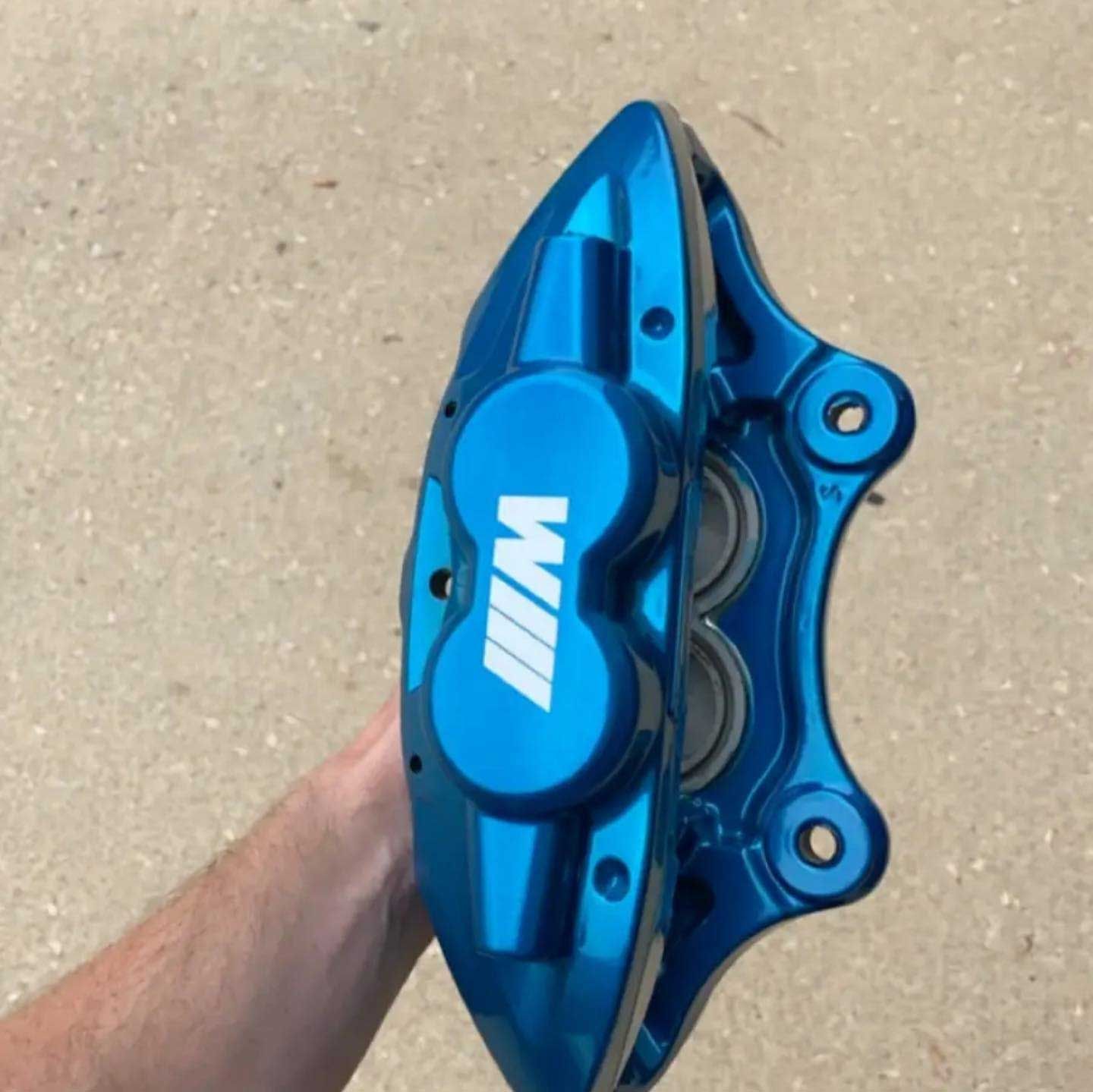 A blue BMW M brake caliper held by a person. The caliper has white 
