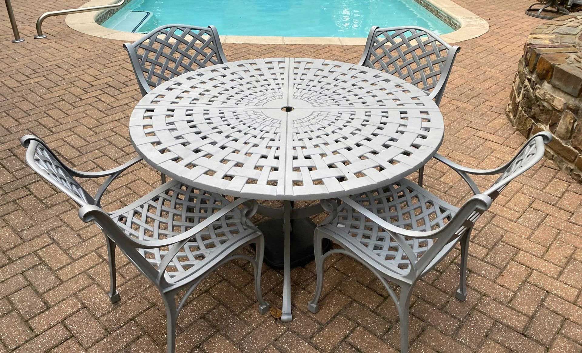 Round metal patio table and four chairs on a brick patio by a swimming pool.