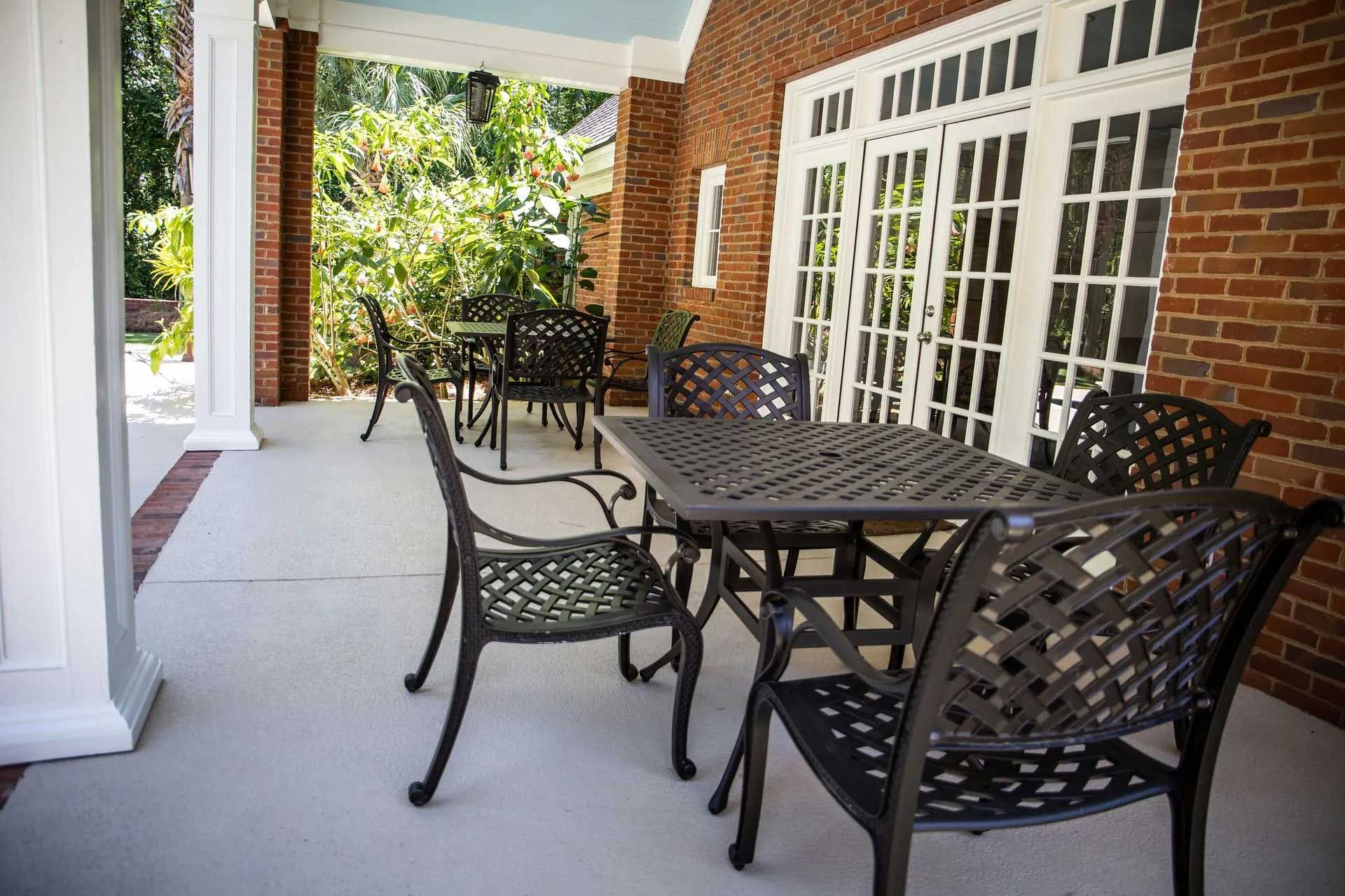 Patio with black metal tables and chairs; red brick wall, white columns, and double doors.