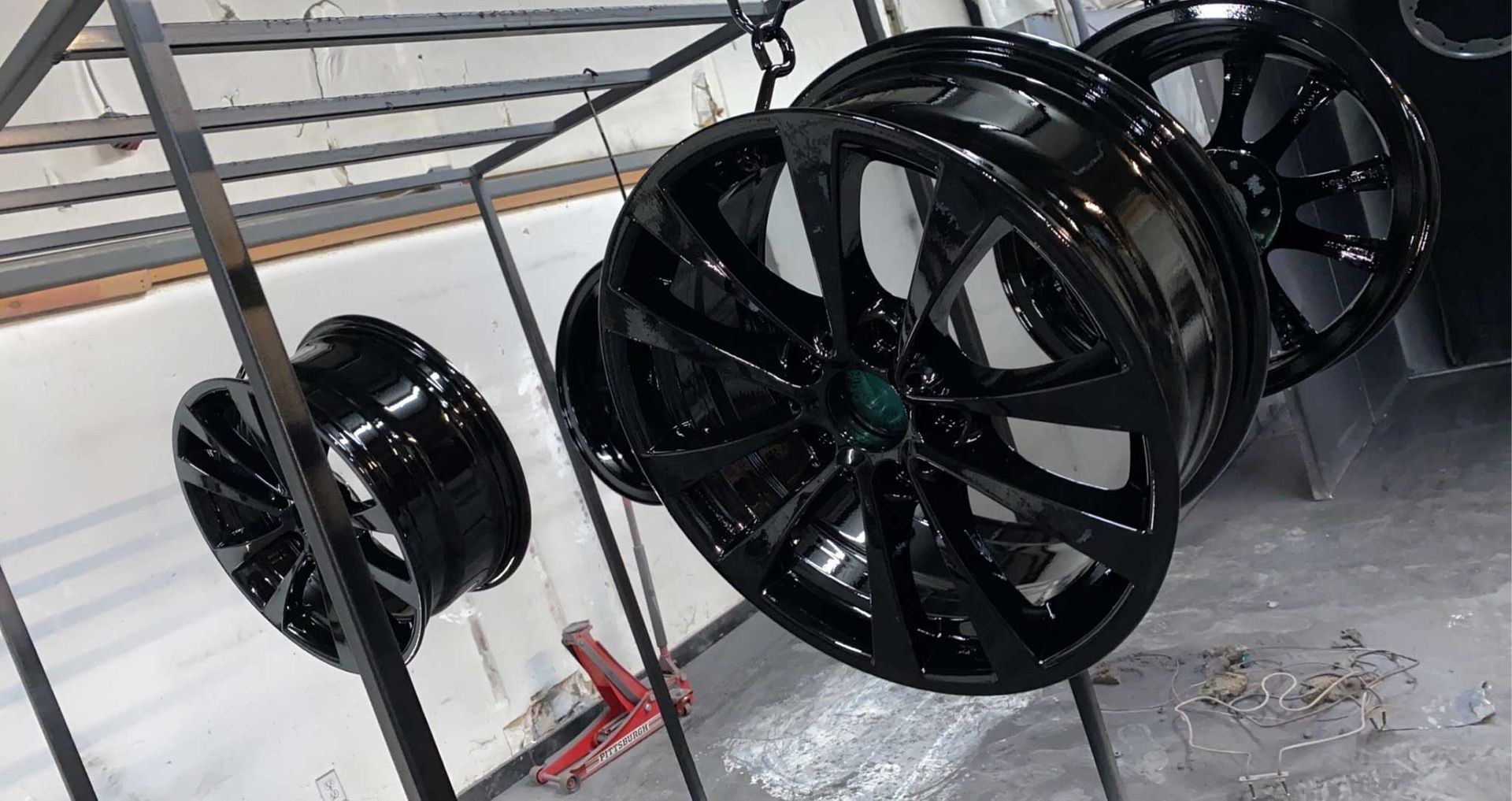 Black alloy wheels hanging to dry, inside a shop.