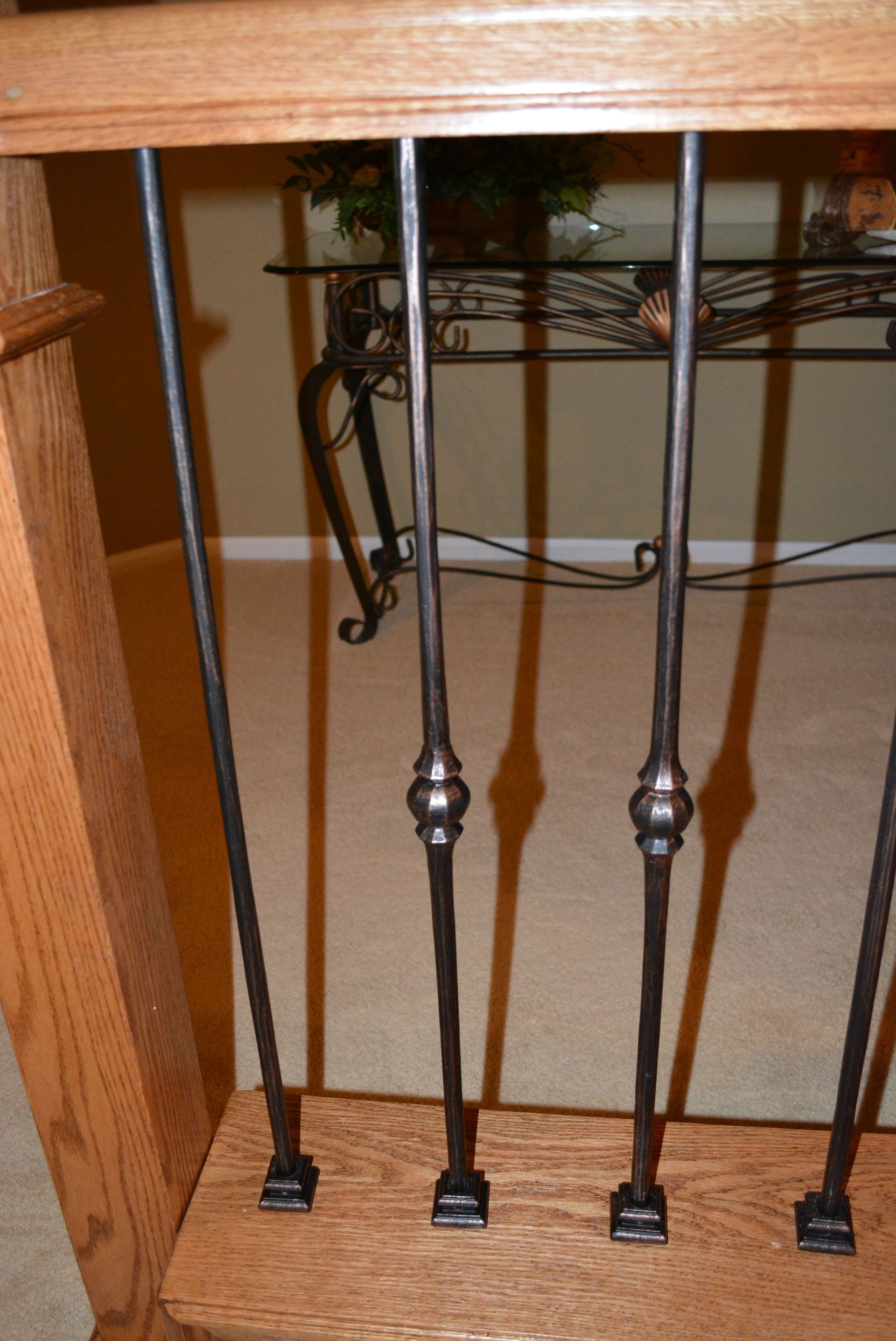A wrought iron railing on a wooden staircase next to a glass table.