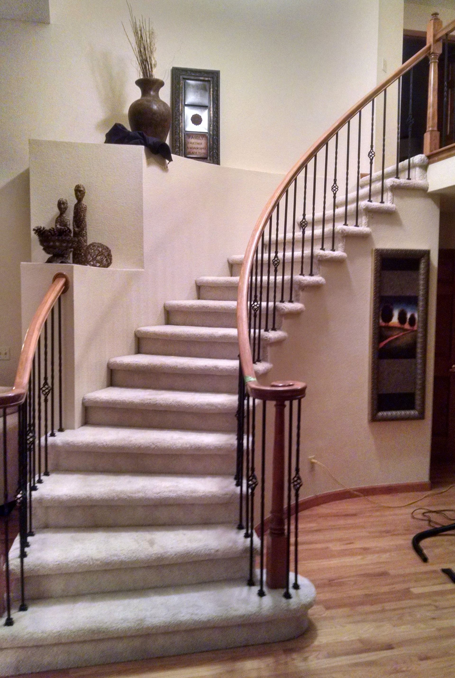 A curved staircase with carpeted steps and a wooden railing
