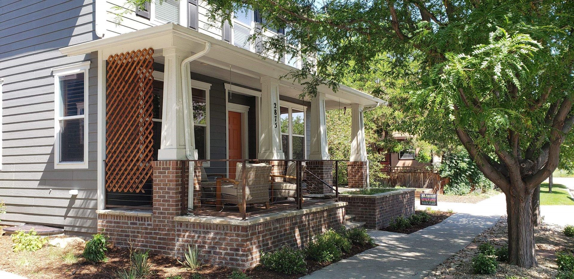 A house with a large porch and a tree in front of it.