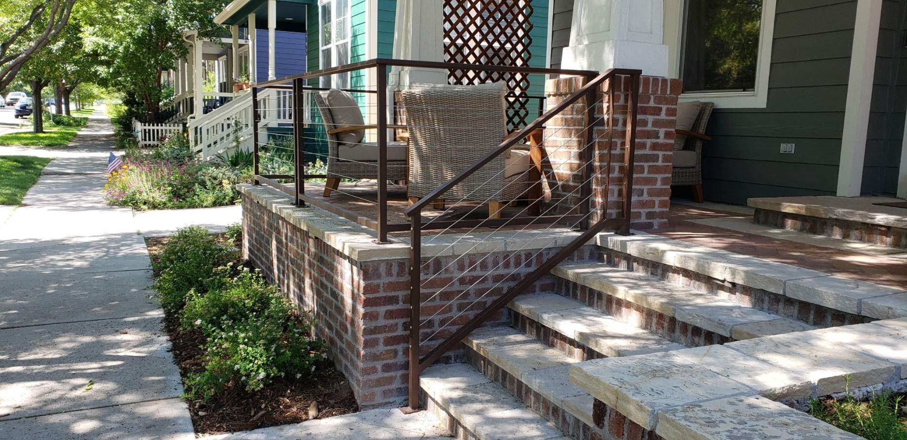 A brick porch with a metal railing and stairs leading up to it.