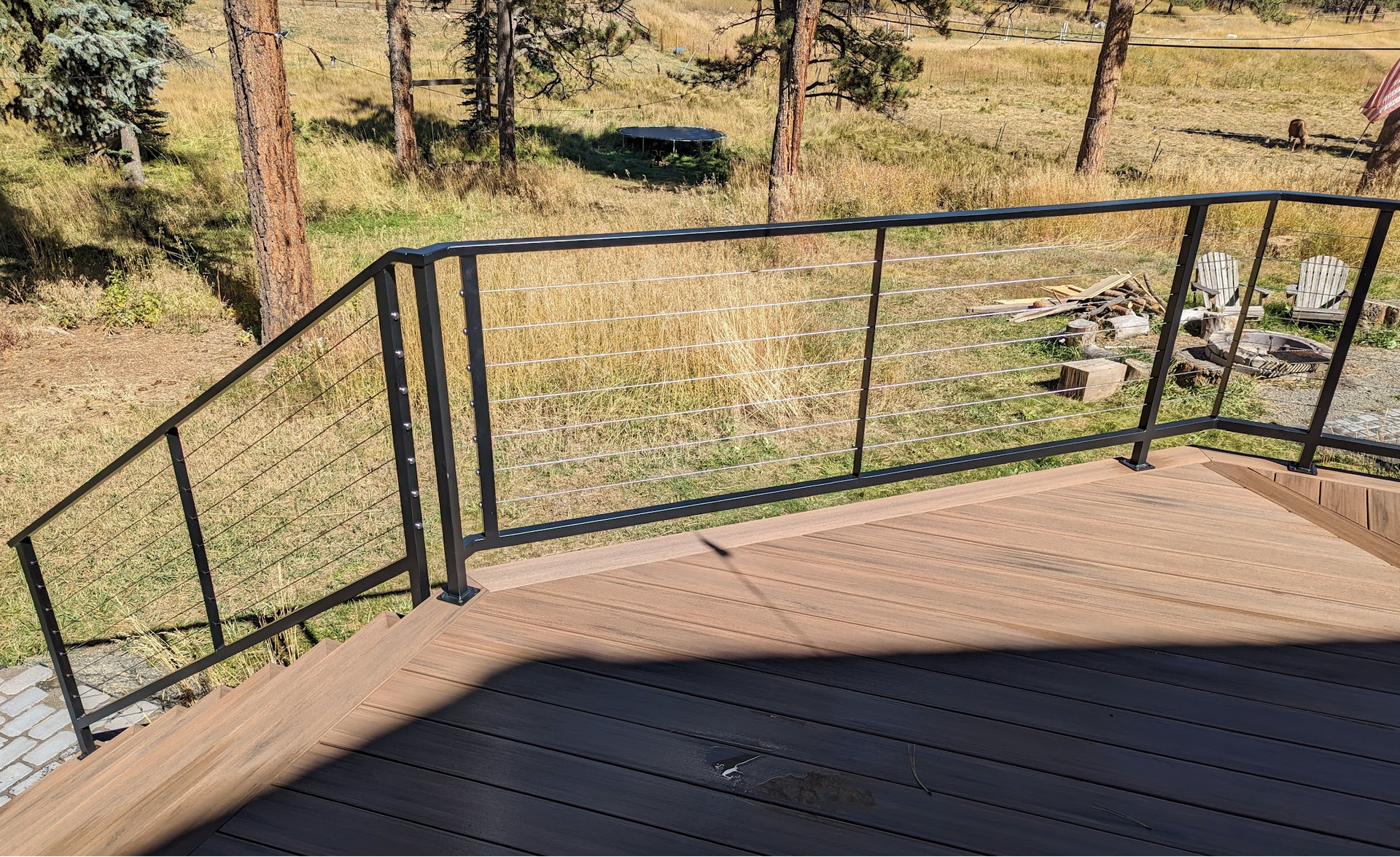 A wooden deck with a metal railing and trees in the background.
