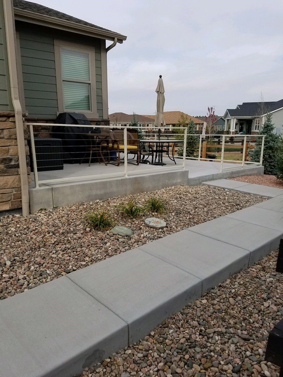 A concrete walkway leading to a deck with a stainless steel railing.