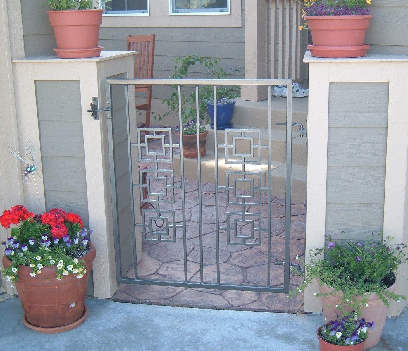 A gate with a geometric design is surrounded by potted plants