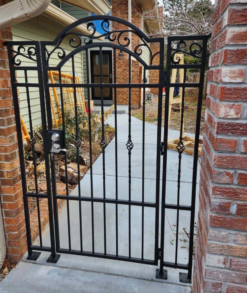 A wrought iron gate is sitting next to a brick wall.